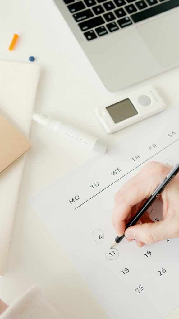pexels-photo-6823398-6823398 A person marking dates on a calendar, with a glucometer and laptop nearby, suggesting diabetes monitoring.